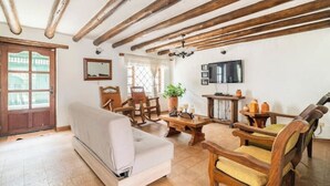 A living room with a sofa, wooden chairs, a coffee table, and a television mounted on the wall.