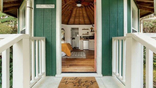 Eine Holzveranda mit einer grünen Tür, einem Schild mit der Aufschrift 'Calle Hondu' und einer Fußmatte mit der Aufschrift 'nur gute Vibes'.