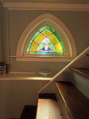 Ein farbiges Glasfenster mit geometrischem Muster, eine Holztreppe und eine klare Glasschale auf einem Podest.