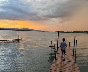 Eine hölzerne Mole, die sich in ruhiges Wasser erstreckt, mit einem Sonnenuntergang im Hintergrund.