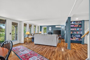Un salón amplio con sofá, televisor, estantería y ventanas grandes.