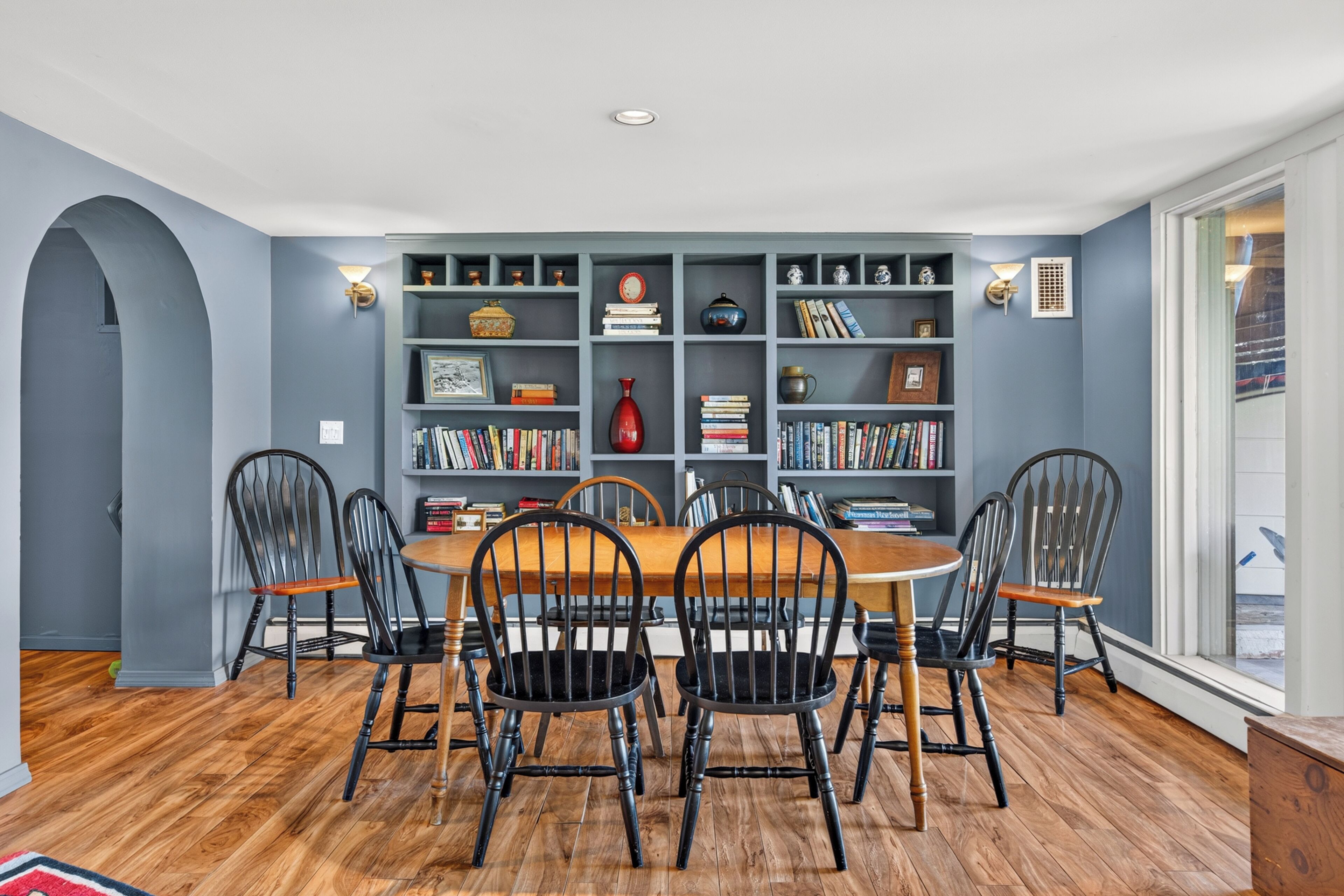 A dining room with a wooden table and chairs, surrounded by bookshelves filled with books and decorative items.