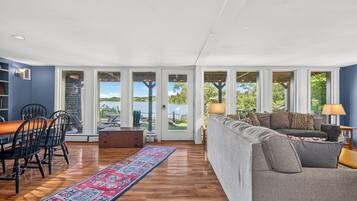 Un salón amplio con una mesa de comedor de madera, un sofá gris y vistas a un lago a través de amplios ventanales.