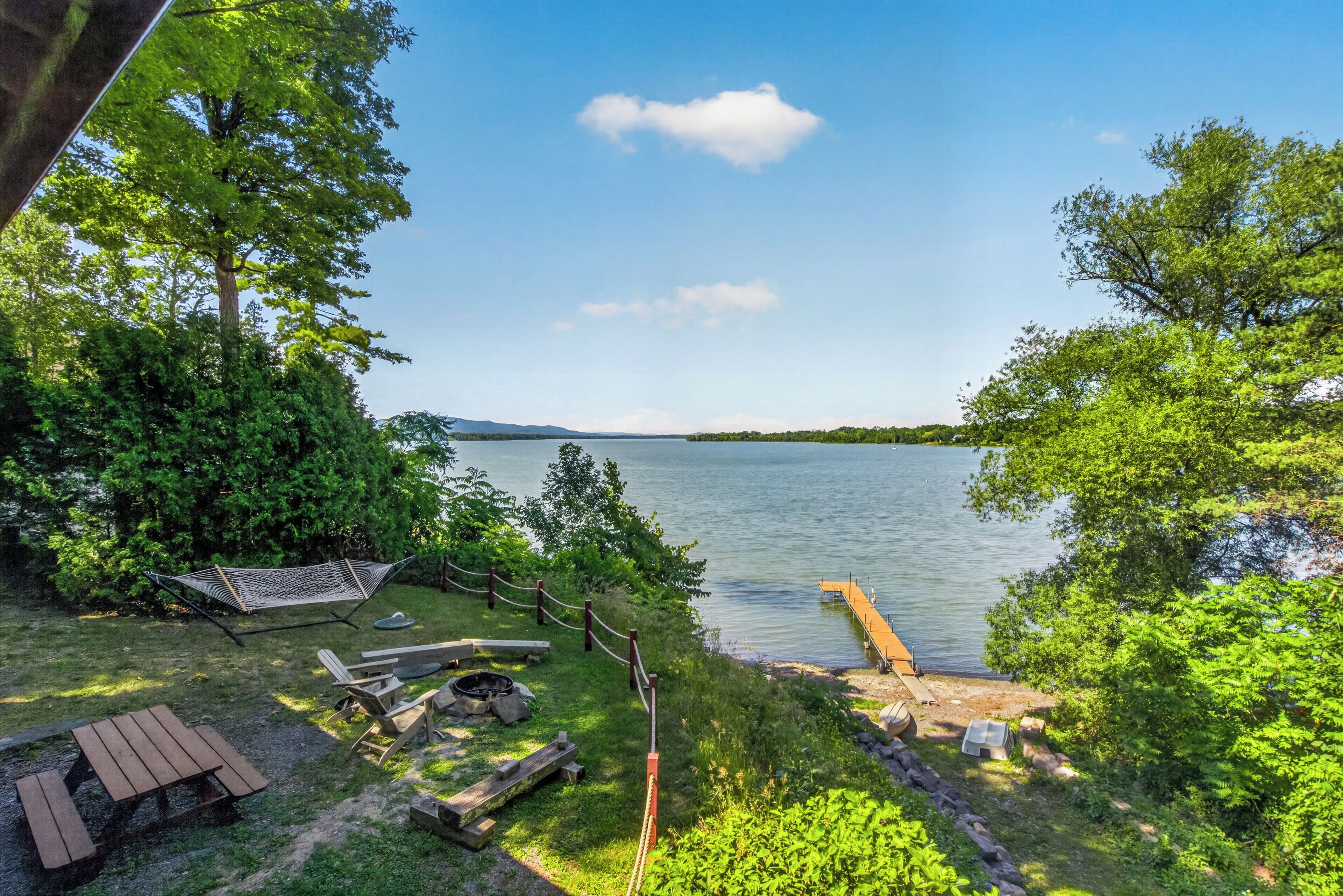 A lakeside outdoor area with a hammock, picnic table, and fire pit.