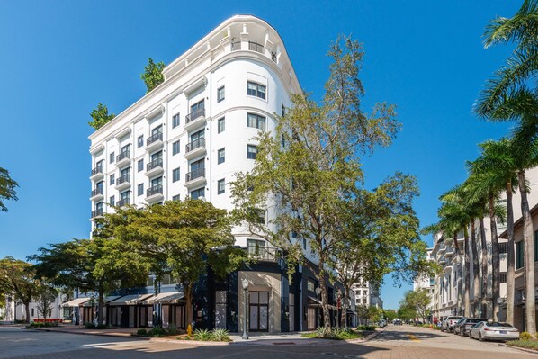 A multi-story hotel with balconies, a curved facade, and a street view with parked cars and trees.