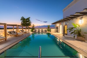 A swimming pool with lounge chairs and a view of the sunset.