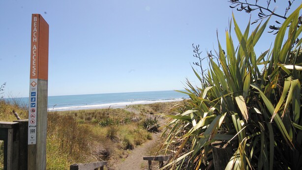 A wooden pathway leading to a beach with a sign indicating beach access.