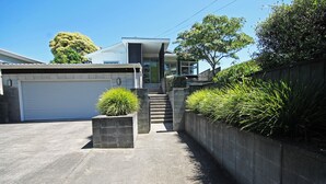 A modern house with a garage, a staircase leading to the entrance, and a concrete wall with plants.