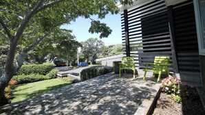 A wooden deck with two green chairs, a hedge, and a building with horizontal slats.