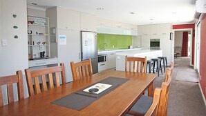 A modern kitchen with white cabinets, a green backsplash, and a dining area with a wooden table and chairs.