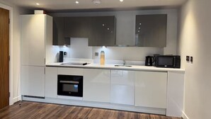 A modern kitchen with white cabinetry, a built-in oven, a microwave, and a coffee maker. - Luxury 2-Bed Apartment | Gym | Jewellery Quarter (Birmingham)