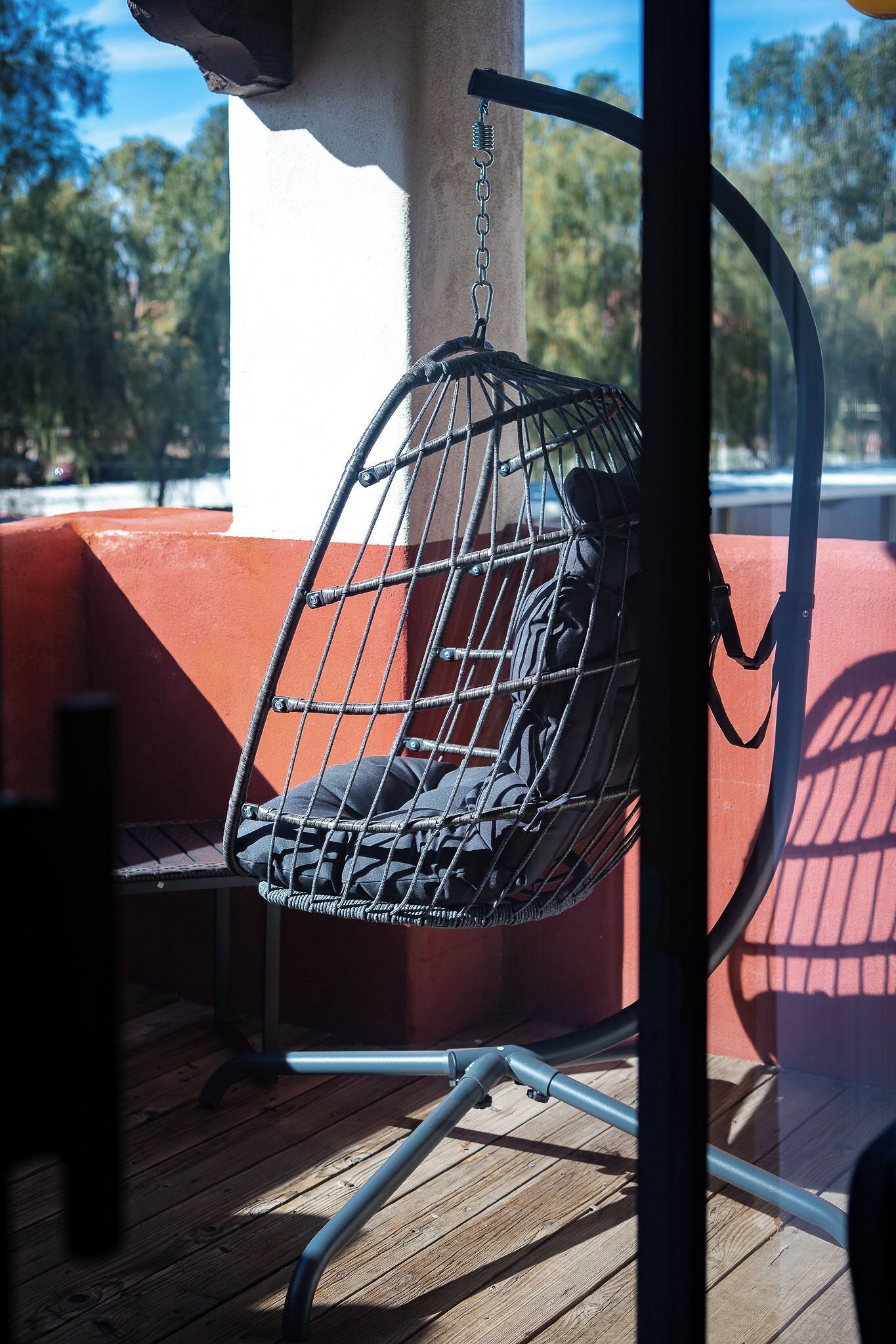 A wicker chair with a cushion hanging from a metal frame, attached to a wall.