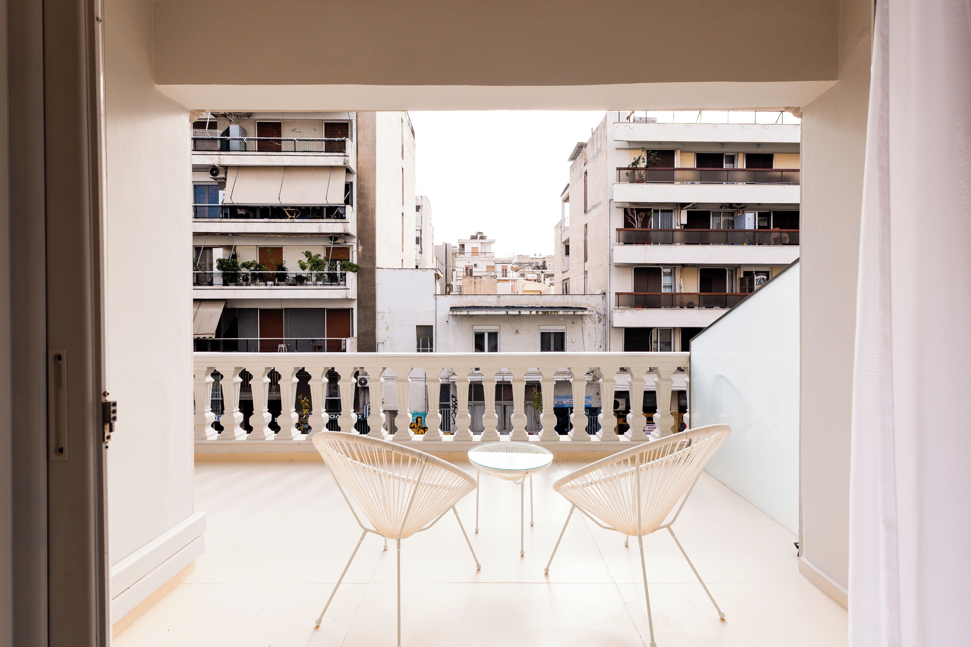 A balcony with two chairs and a table, overlooking a residential area with multiple buildings.