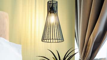 A neatly made bed with a white pillow, a potted plant on a wooden nightstand, and a hanging light fixture.
