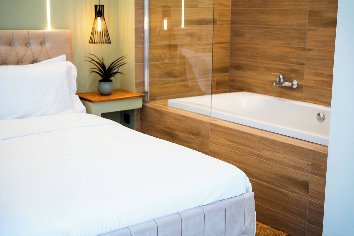Um quarto moderno com uma cama grande, uma mesa de cabeceira com uma planta e uma banheira de vidro.