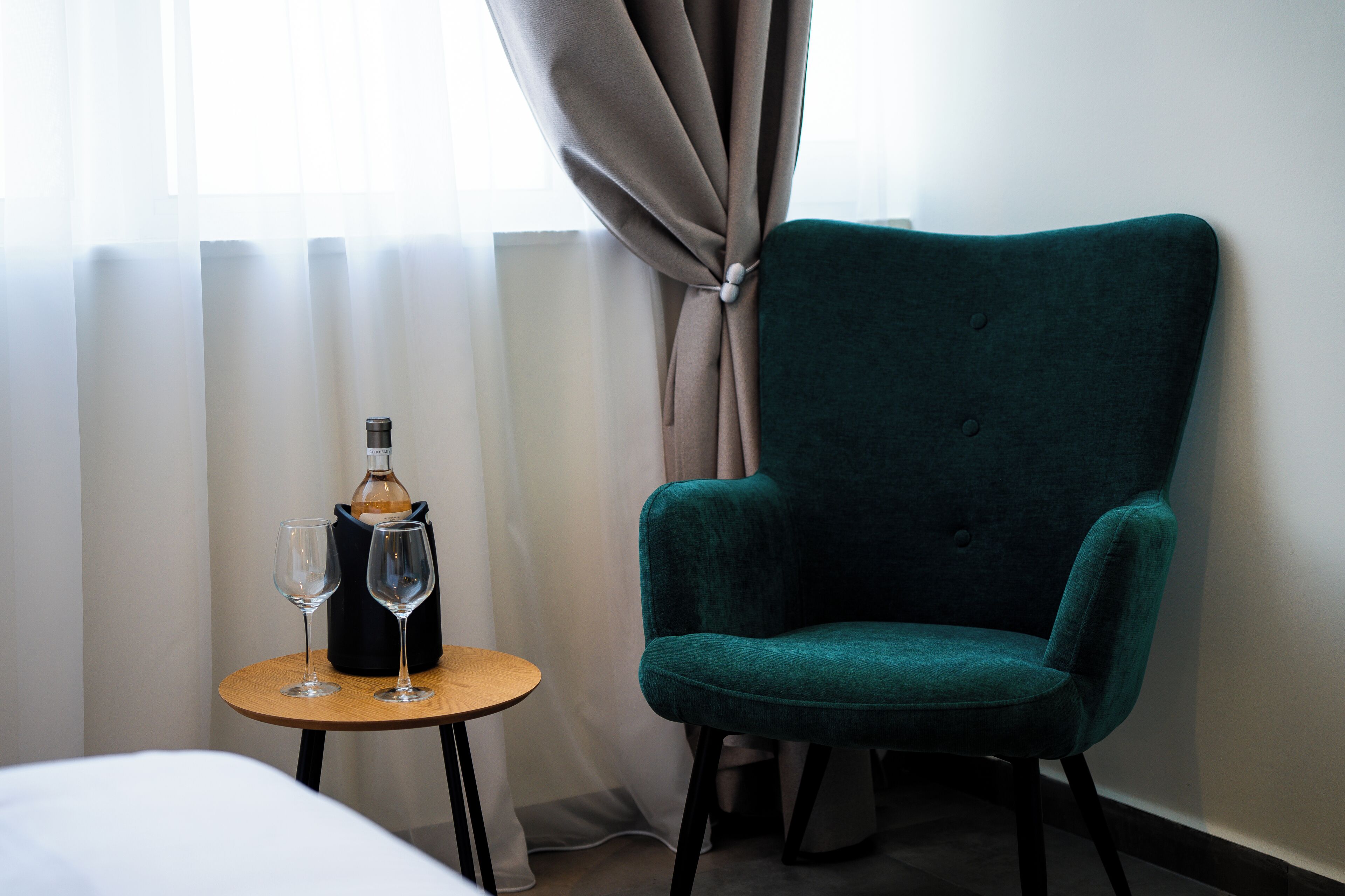 A teal armchair next to a small table with two wine glasses and a bottle.