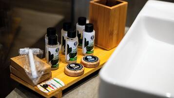 Una encimera de baño con varios artículos de aseo, incluyendo botellas de champú tónico verde y un estuche de madera.