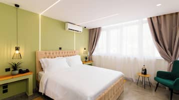 A modern bedroom with a large bed, bedside tables, a green armchair, and a small table with a bottle and glass.