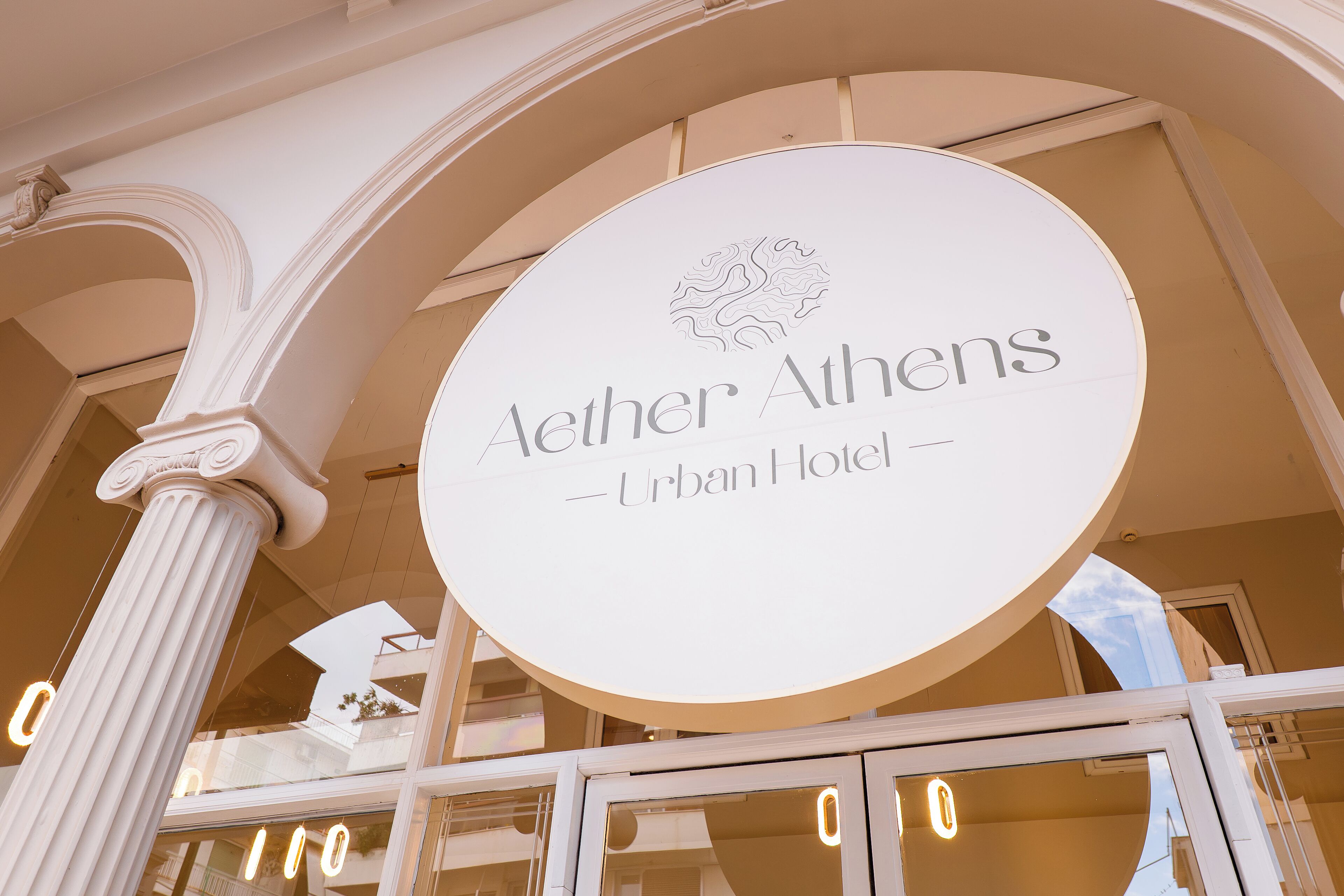 A circular sign with the text "Aether Athens - Urban Hotel" and a lion emblem.
