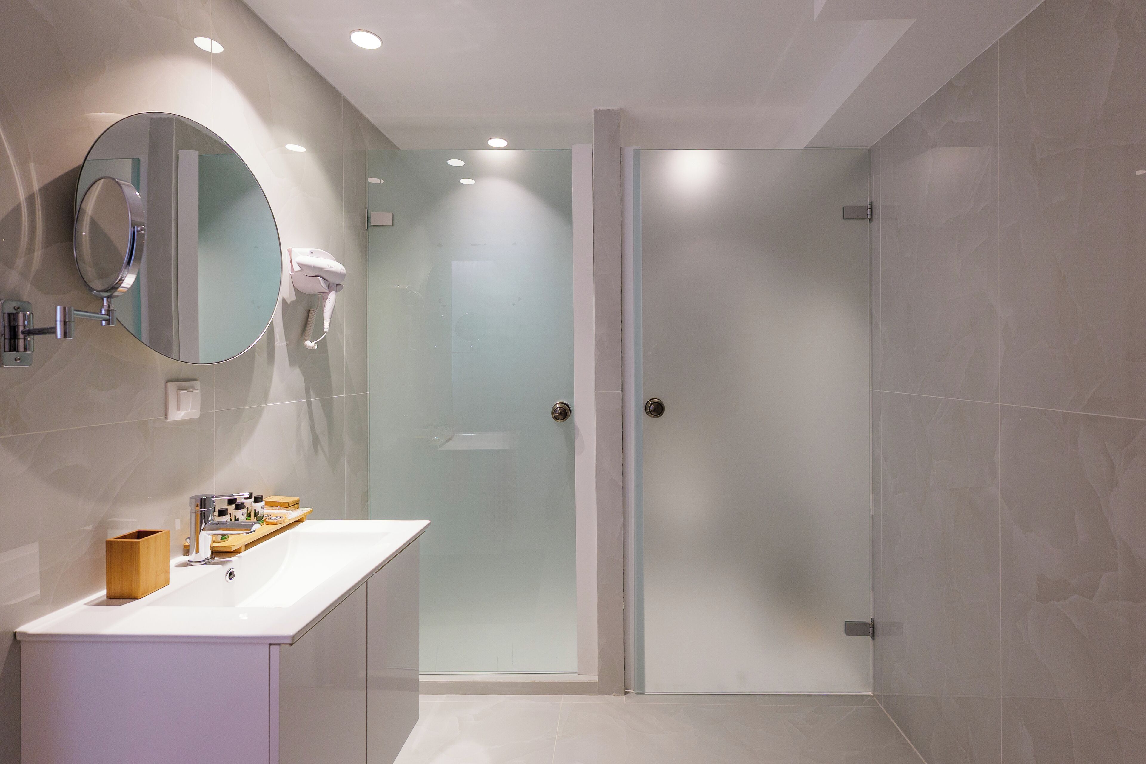 A modern bathroom with a glass shower enclosure, a round mirror, and a white vanity.