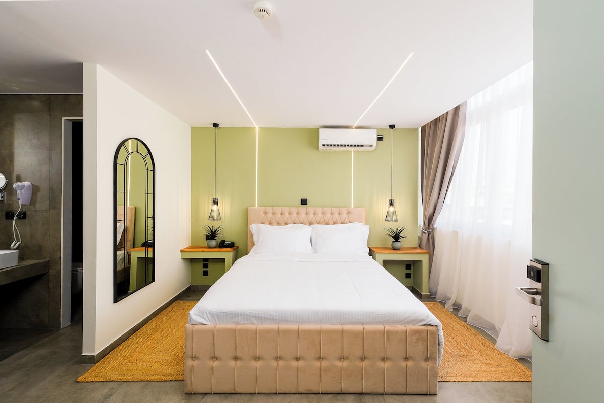 Quarto moderno com uma cama grande, mesas de cabeceira, um espelho e um aparelho de ar condicionado.