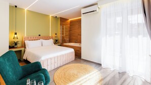 A modern hotel room with a bed, a green armchair, a round woven rug, a bathtub, and sheer curtains.