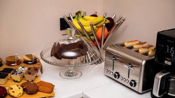 A kitchen counter with a cake on a glass stand, a toaster, and a fruit basket.
