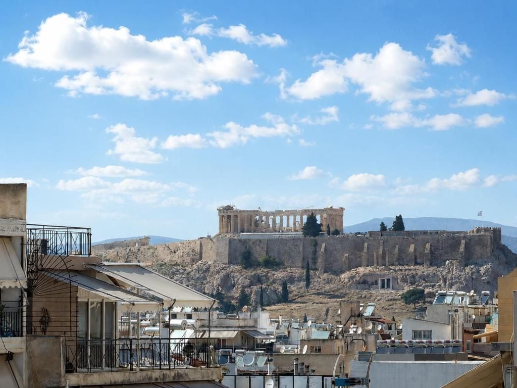 A view of a historic site with ancient ruins, modern buildings, and a clear sky.