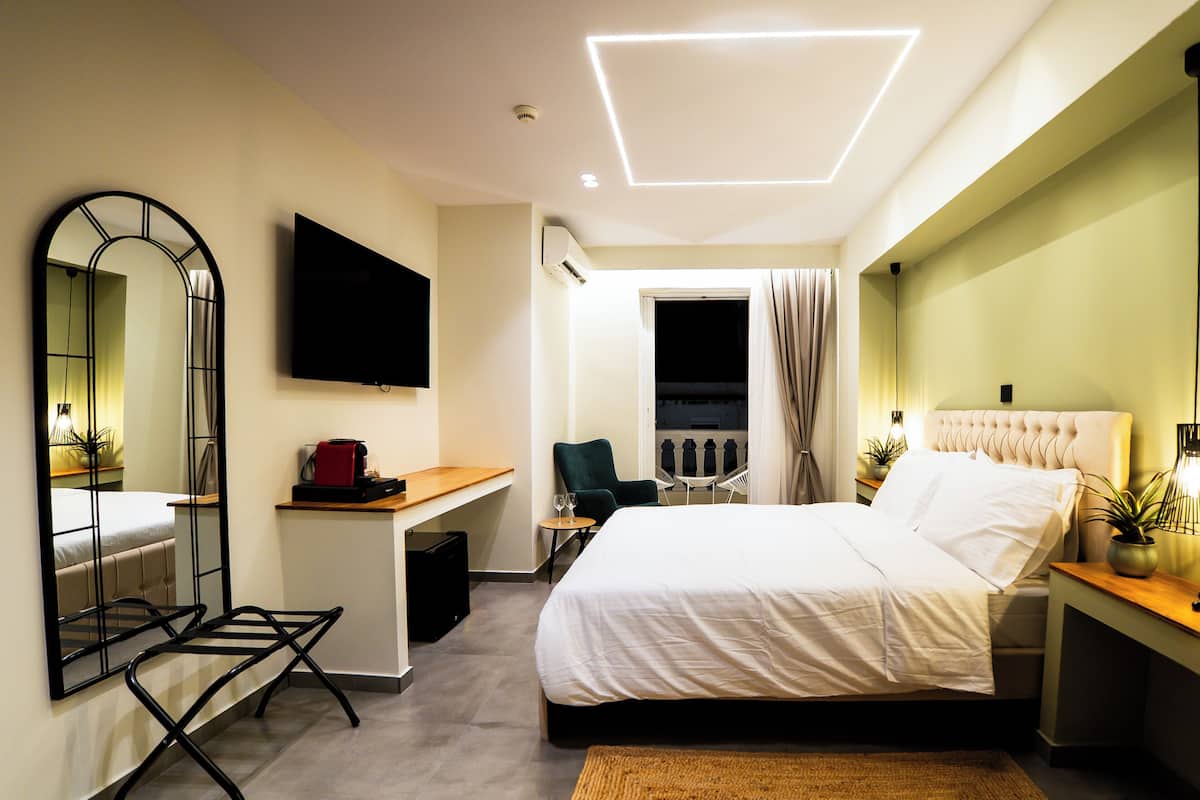 Quarto de hotel moderno com uma cama grande, uma escrivaninha, uma cadeira, uma televisão e uma janela com cortinas.