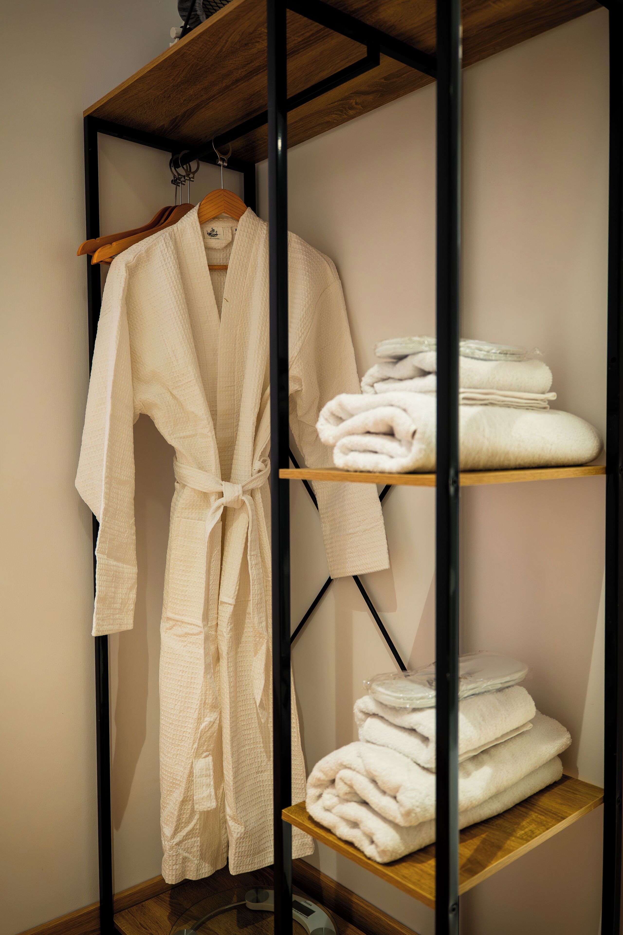 A robe hanging on a rack with folded towels on shelves.