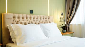 A neatly made bed with white linens, a tufted headboard, and a bedside table with a potted plant.