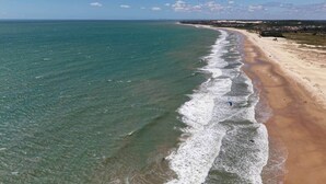 Vista aerea di una spiaggia con acque limpide, una riva sabbiosa e una città in lontananza.