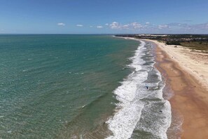 Une vue aérienne d’une plage avec une eau cristalline, un rivage sablonneux et une ville située au loin.