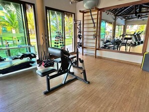 A gym with exercise equipment, large windows, and a view of palm trees. - Bungalow Frente Mar N 101 (Caucaia)