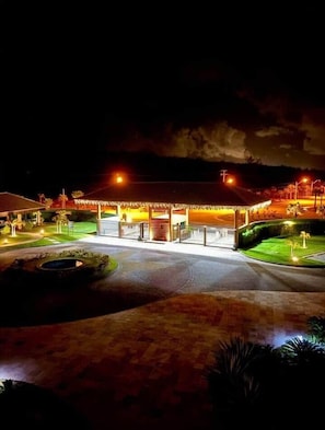Un hotel con un camino pavimentado, una entrada bien iluminada y un área ajardinada con palmeras.