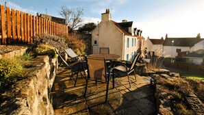 Eine Terrasse mit Tisch und Stühlen, eine Steinmauer und ein Holzzaun.