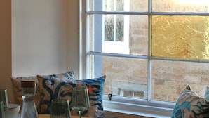 Un comedor con una mesa dispuesta para cuatro personas, una ventana que ofrece vistas a un edificio de ladrillo y lámparas colgantes.