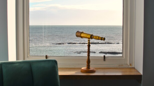 Un telescopio en el alféizar de una ventana con vistas al mar.