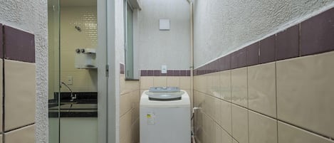 A compact bathroom with a washing machine, a glass shower enclosure, and tiled walls.