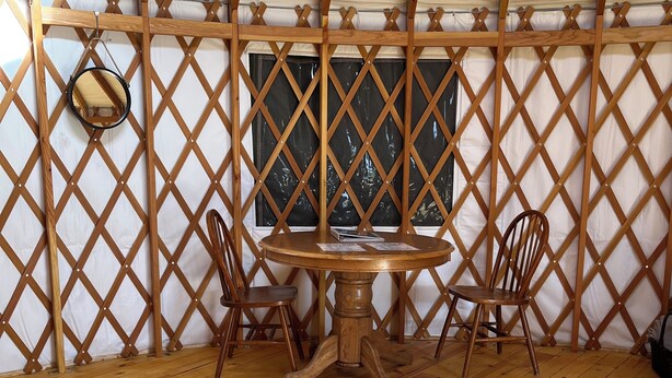 A wooden table with two chairs in a tent-like room with a lattice wall and a window. - North Star Yurt at Whiterock Conservancy (Coon Rapids)