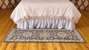 A bedroom with a bed, a wooden floor, a patterned rug, and a lattice wall. - North Star Yurt at Whiterock Conservancy (Coon Rapids)