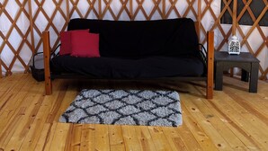 A cozy interior with a wooden floor, a black sofa with red cushions, a patterned rug, and a small table with a decorative item. - North Star Yurt at Whiterock Conservancy (Coon Rapids)