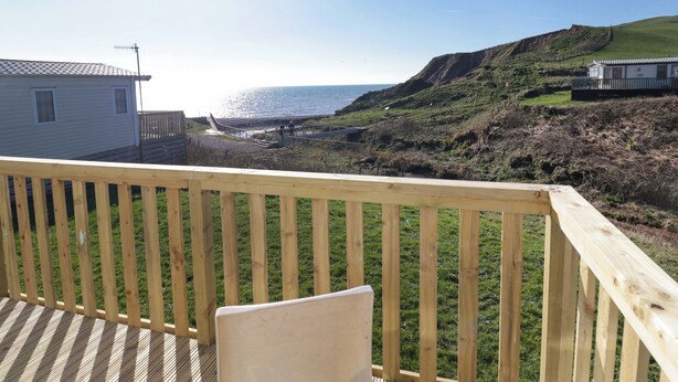 A wooden deck with a view of the ocean and a grassy hillside. - Guillemot (St Bees)