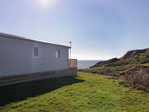 Une maison mobile dotée d’une terrasse donnant sur une zone herbeuse et un plan d’eau.