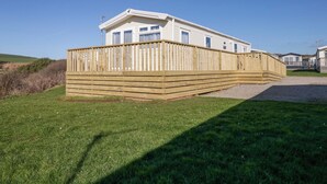 A mobile home with a wooden deck and a fenced yard. - Guillemot (St Bees)