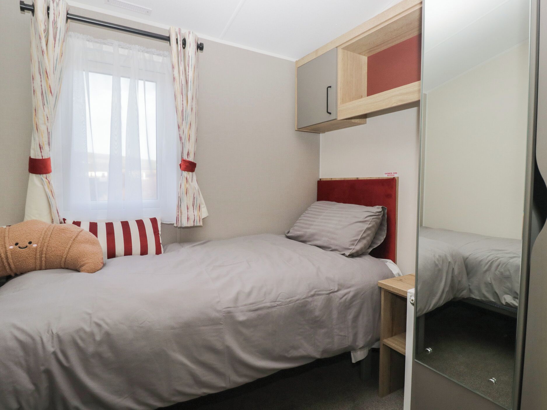 Un lit simple avec une tête de lit rouge, une table de chevet et un miroir.