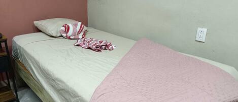 A single bed with a white mattress, a pink blanket, and a striped pillow.