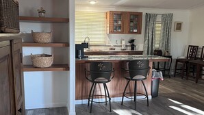 A kitchen with wooden cabinets, a marble countertop, and two bar stools. - Gator Camp 2.7 off the rim of Lake Okeechobee Buckhead Ridge (Okeechobee)