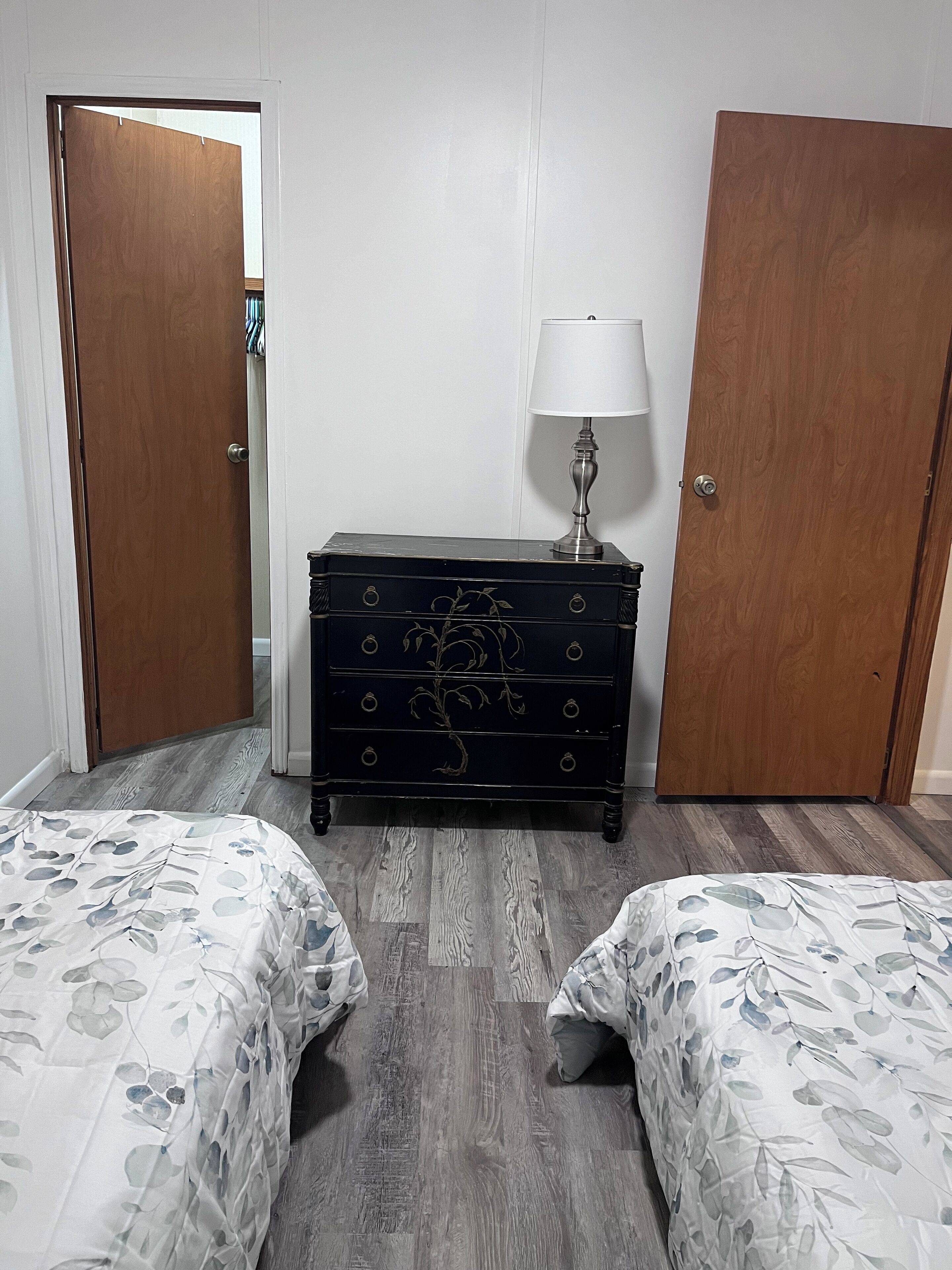 A room with two beds, a dresser, a lamp, and two doors.