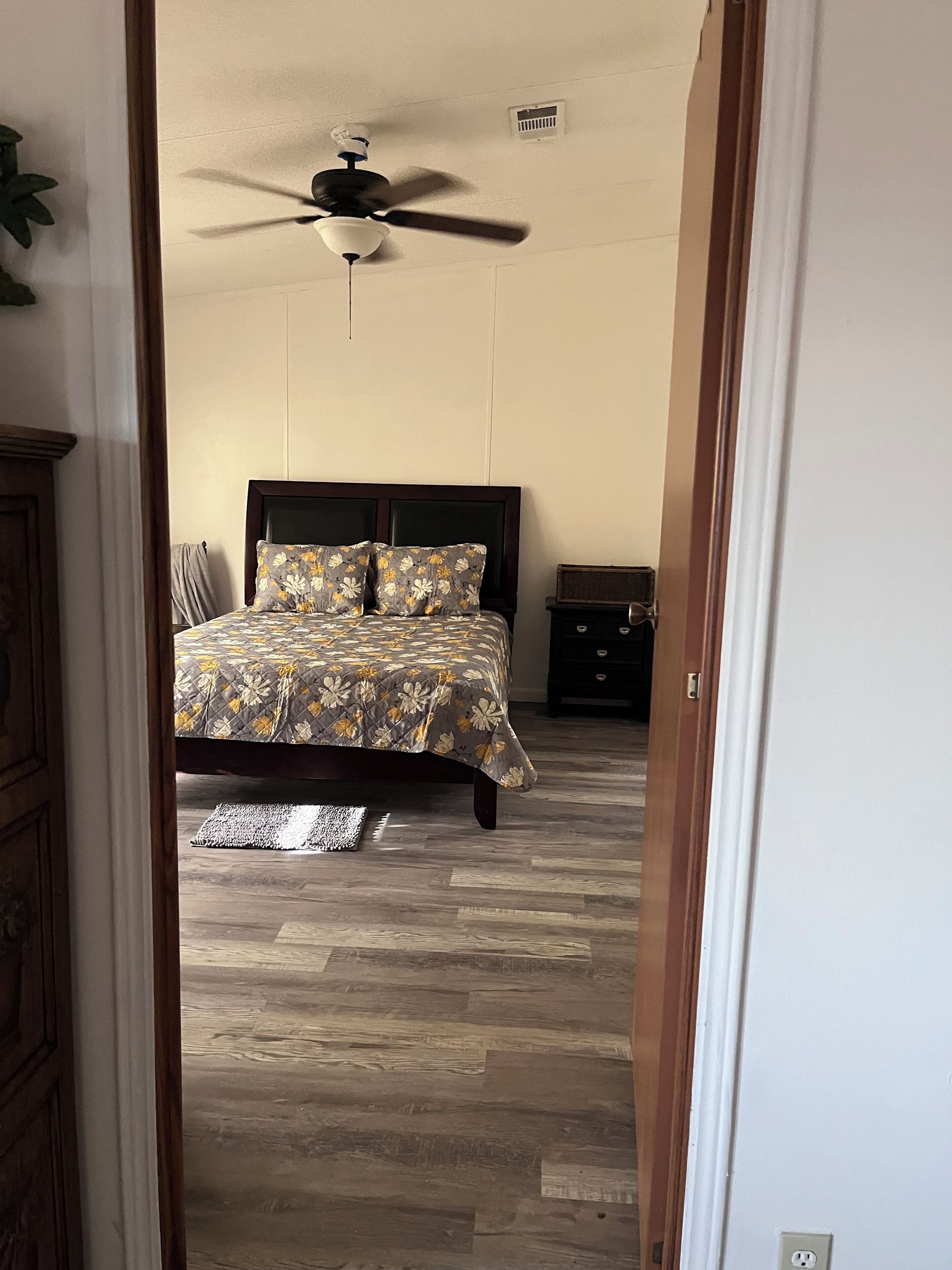 A bedroom with a bed, a ceiling fan, a nightstand, and a wooden floor.